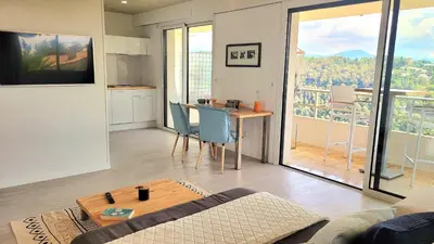 a living room with a table and a kitchen with a balcony at Studio climatisé vue imprenable wifi in Vence