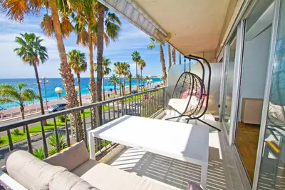 a balcony with a couch and palm trees and the ocean at Luxury sea front suite Promenade in Nice