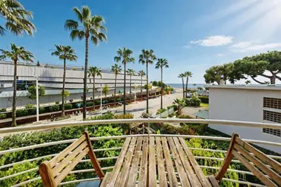 a wooden bench on a balcony with palm trees at Beautiful flat with balcony and sea view in Saint-Laurent-du-Var