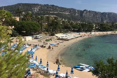 a beach with umbrellas and people in the water at Pool , 150m to beach, seaview in Villefranche-sur-Mer