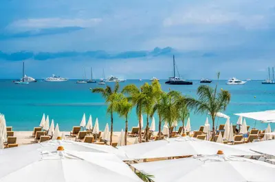 a beach with white umbrellas and palm trees and boats at Le BASHKIR - SPACIEUX AVEC TERRASSE - WIFI - prés mer et aéroport - Tram et supermarchés in Nice