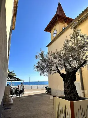 a building with a clock tower with a tree in a box at Orangers - Bord de mer - Studio cosy 4 personnes in Cagnes-sur-Mer
