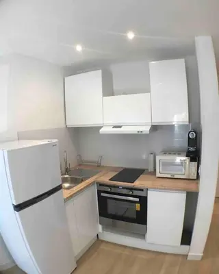 a small kitchen with white cabinets and a refrigerator at Nice bas Cimiez- Coquet F1, climatisée, Parking in Nice