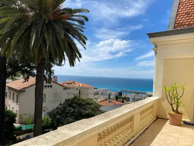 a balcony with a palm tree and a view of the ocean at PALMERAIE - Magnifique appartement d'époque avec Vue Mer 4 personnes avec terrasse Le Port Nice in Nice