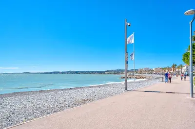 a beach with a flag and people walking on the beach at Appartement à 100m de la plage, climatisé in Cagnes-sur-Mer