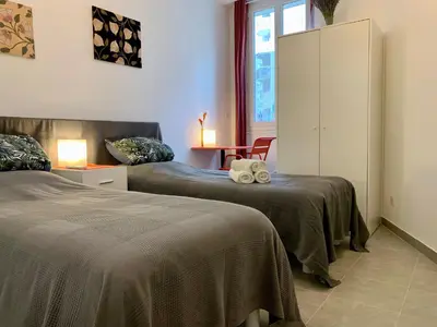 a bedroom with two beds and a table with a chair at ApartHotel Riviera - MAISON DU GRAND SUD - Confortable petit 3 pièces - Promenade des Anglais in Nice