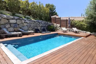 a swimming pool with a wooden deck and a stone wall at VILLA MODERNE PISCINE JACUZZi in Nice