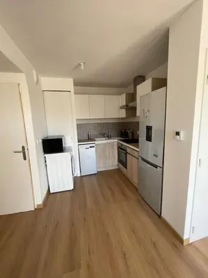 a large kitchen with white appliances and wooden floors at Appartement avec piscine in Saint-Laurent-du-Var
