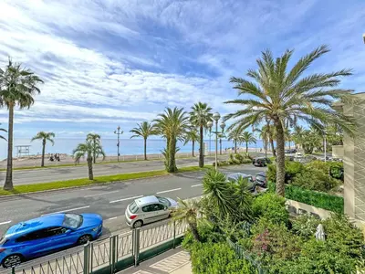 a street with parked cars and palm trees and the ocean at Gorgeous Oceanfront Apartment Promenade in Nice