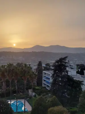a sunset over a city with palm trees and a building at Terrasses de la Corniche, 2p 65m2 spacieux, terrasses mer & montagne, piscine et parking privé in Nice