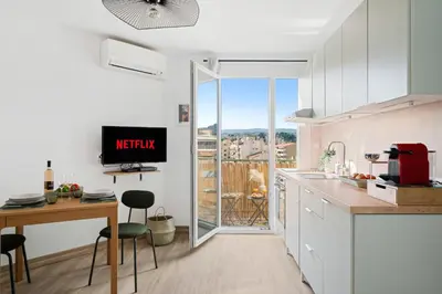 a kitchen with white cabinets and a table with a tv at Vista Nissa - À Quelques Pas du Port in Nice