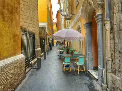 an alley with tables and chairs with an umbrella at Cosy appartement, moderne, fuchsia, industriel in Nice