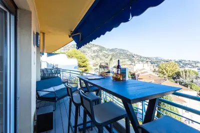 a blue table and chairs on a balcony with a view at Esterel AP4431 By Riviera Holiday Homes in Villefranche-sur-Mer