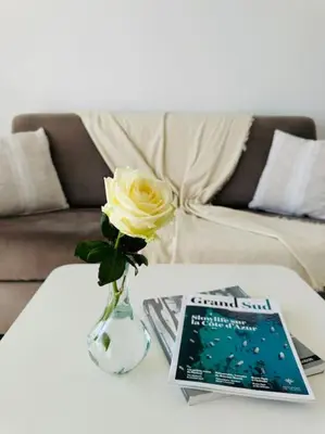 a vase with a yellow rose and a book on a table at Évasion Mer & Vue Imprenable in Saint-Laurent-du-Var