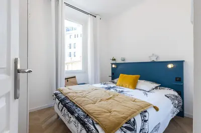 a bedroom with a bed with a blue headboard and a window at 37 MASSENA LOT 2 - Superbe 3 pieces - Zone Pietonne - A-C in Nice