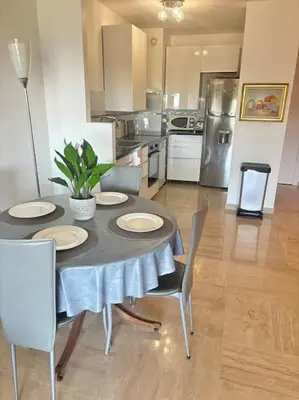 a dining room with a table and chairs and a kitchen at Appartement lumineux Vue Mer, Piscine et tennis in Nice