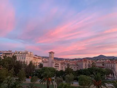 a building with a clock tower in front of a sunset at 2 chambres, balcons, vue imprenable, climatisation - PALACE BLEU in Nice