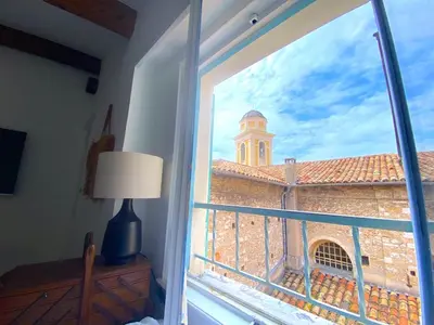 a window with a view of a building with a tower at PERCHOIR AP4443 By Riviera Holiday Homes in Villefranche-sur-Mer