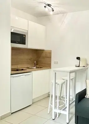 a kitchen with white cabinets and a table with stools at Nid douillet rénové et tramway à 1 min in Nice