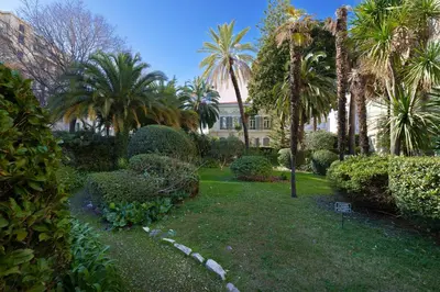 a garden with palm trees and bushes in front of a building at Nice Renting - VICTOR - Historic Palace Luxury 3 Bedrooms in Nice