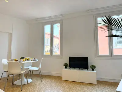 a white living room with a table and a television at Charmant 2 pièces proche mer in Nice
