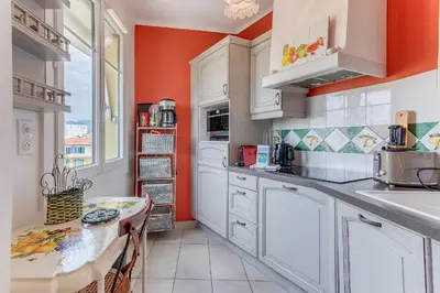 a kitchen with white cabinets and an orange wall at LE PAIROLIERE AP4461 by Riviera Holiday Homes in Nice