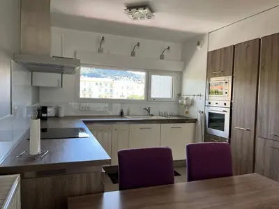 a kitchen with white cabinets and purple chairs at 3 pièces central au pied de la promenade du paillon in Nice