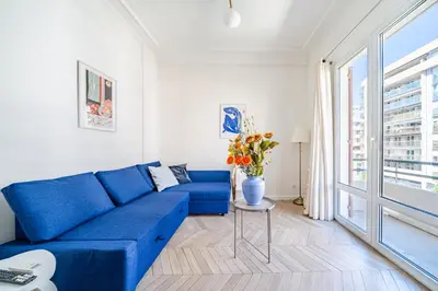 a blue couch in a white living room with a window at Studio moderne proche mer - Balcon et Climatisé in Nice