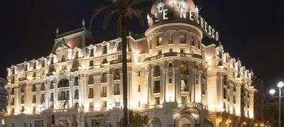 a lit up building with a palm tree in front of it at Nid perché avec aperçu mer Tout à pied ! in Nice