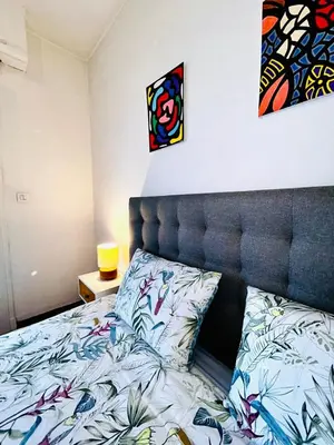 a bedroom with a bed with a headboard and paintings on the wall at Azure Horizons Seaside Escape in Beaulieu-sur-Mer