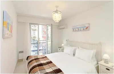 a white bedroom with a bed and a chandelier at 2 pièces centre ville-Balcon in Nice