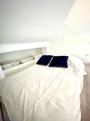 a white bed with two blue pillows on it at Studio close to Main Street and Train Station in Nice