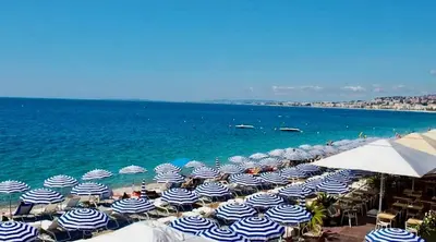 a beach with blue and white umbrellas and the ocean at Rossetti in Nice