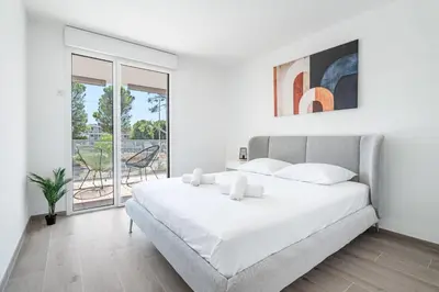 a white bedroom with a large bed and a balcony at Appartement Colombier - Welkeys in Saint-Laurent-du-Var