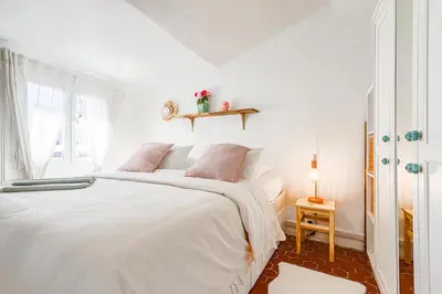 a white bedroom with a white bed with pink pillows at Le Collet - appt climatisé proche plage in Nice