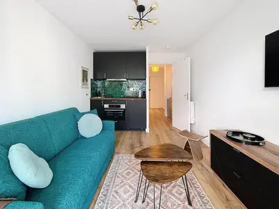 a living room with a blue couch and a kitchen at Sunny studio on a high floor with terrace in Nice