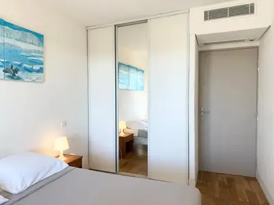 a bedroom with white walls and a bed and a mirror at 2 pièces cosy avec grande terrasse & piscine in Cagnes-sur-Mer