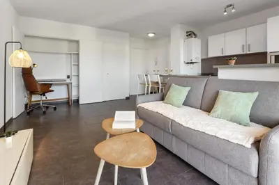 a living room with a gray couch and a kitchen at Le Galion - City centre - Bright - AC - Parking in Cagnes-sur-Mer