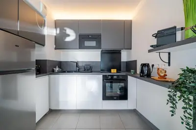 a kitchen with white cabinets and black appliances at Superbe 2 pièces - Piscine et garage in Nice