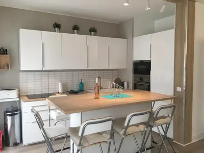 a kitchen with white cabinets and a wooden table with chairs at 3 pièces 10 min de la mer et du tram in Nice