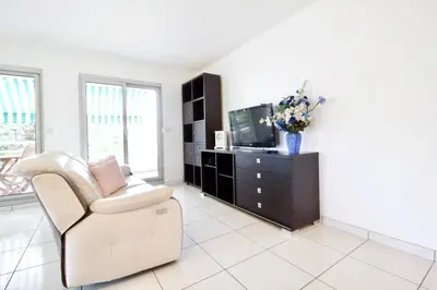 a living room with a chair and a tv at Terrasse, piscine & parking sur la Côte d'Azur in Saint-Laurent-du-Var