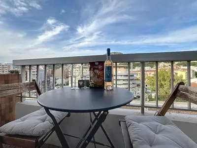 a table on a balcony with a bottle and two chairs at Évasion niçoise à 12 min du port Vue & confort in Nice