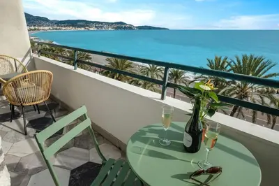 a table with wine glasses and a vase with flowers on a balcony at Baie des Anges in Nice
