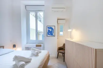 a white bedroom with a bed and a chair at The Apartment with the Garden Studio in Nice