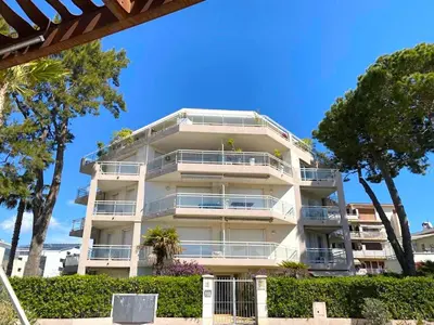 a white apartment building with trees in front of it at Appartement sur la Plage, Le Royal Beach in Saint-Laurent-du-Var