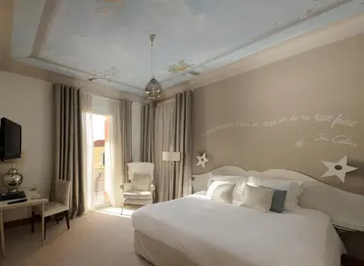 a bedroom with a large white bed and a chair at Welcome Hotel in Villefranche-sur-Mer