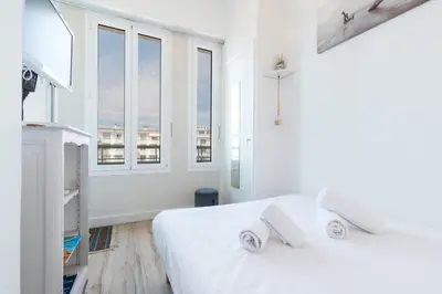 a white bedroom with two white beds and windows at Sea View - Promenade des Anglais 1 Bdr in Nice