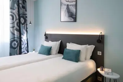 two beds in a hotel room with blue and white pillows at Best Western Alba in Nice