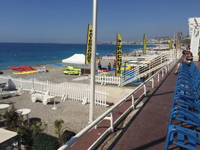 a beach with a white fence and chairs and the ocean at Top Floor Apartment Santa Barbara in Nice