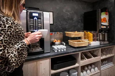a woman is standing in front of a coffee machine at Nemea Appart Hotel Le Lido Cagnes sur Mer in Cagnes-sur-Mer